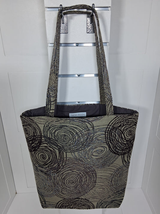 Front: "Handcrafted black swirl tapestry tote bag by Pinpins Designs, front view showing bold circle pattern and long fabric handles