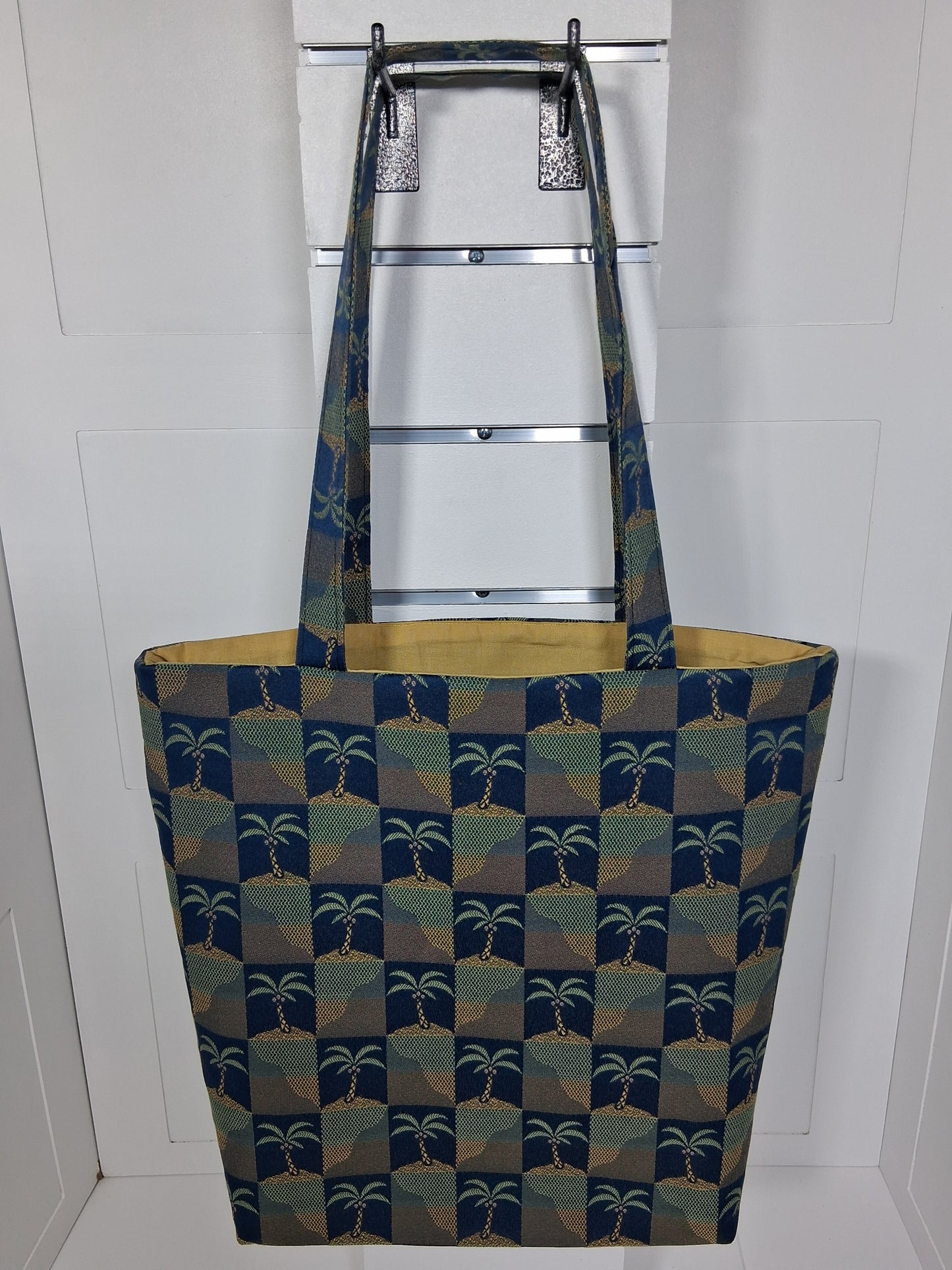 Front: "Handcrafted navy blue and gold palm tree tapestry tote bag by Pinpins Designs, front view showing structured body and long fabric handles"
