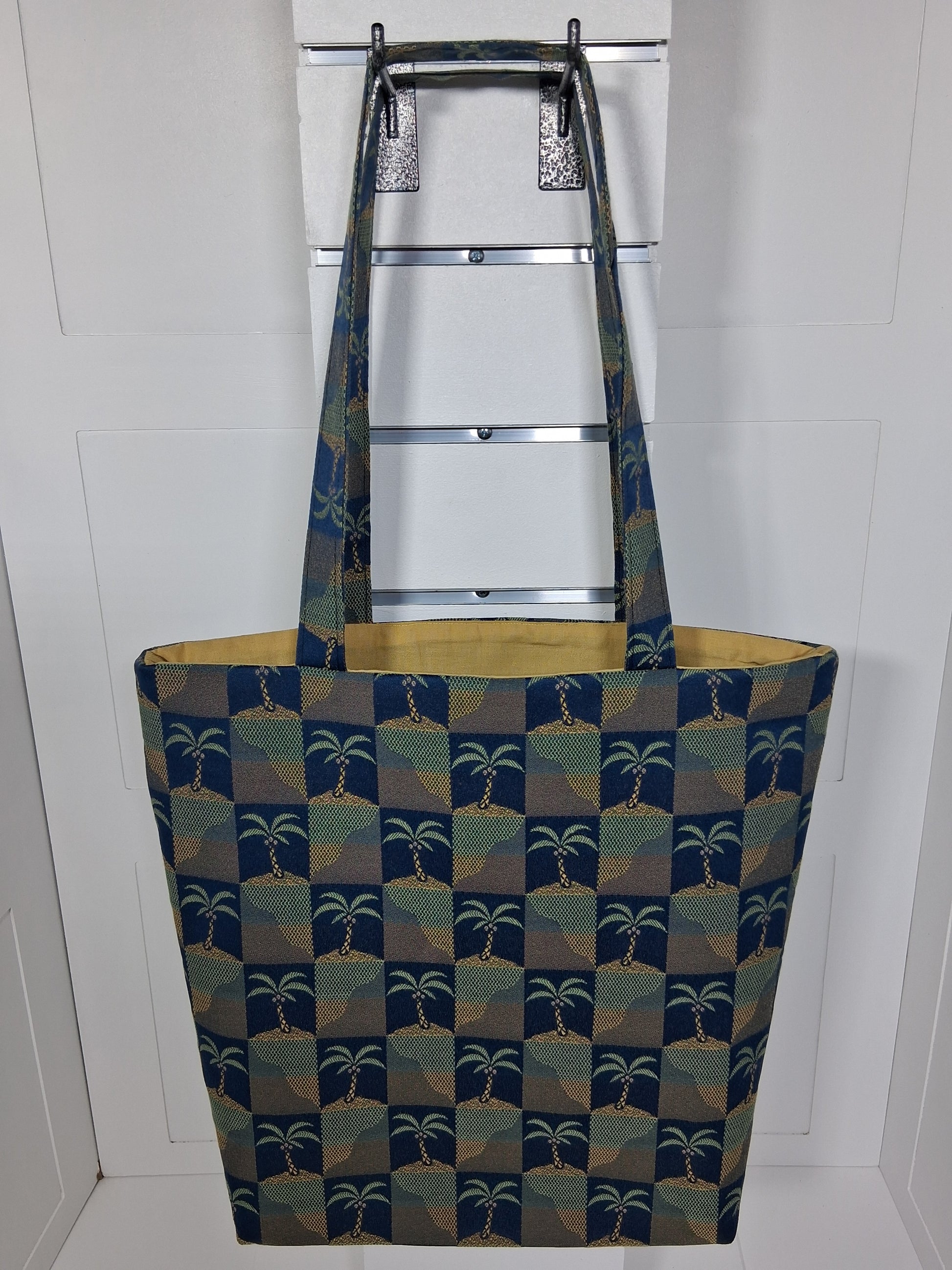 Front: "Handcrafted navy blue and gold palm tree tapestry tote bag by Pinpins Designs, front view showing structured body and long fabric handles"